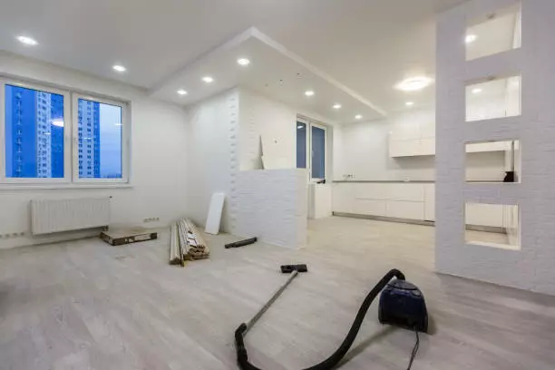 An unfinished modern kitchen and living room interior with construction materials and equipment awaiting a deep cleaning by a bay area cleaning company.