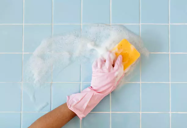 Hand in pink glove cleaning tiled wall with soapy sponge as part of a bay area house cleaning service.