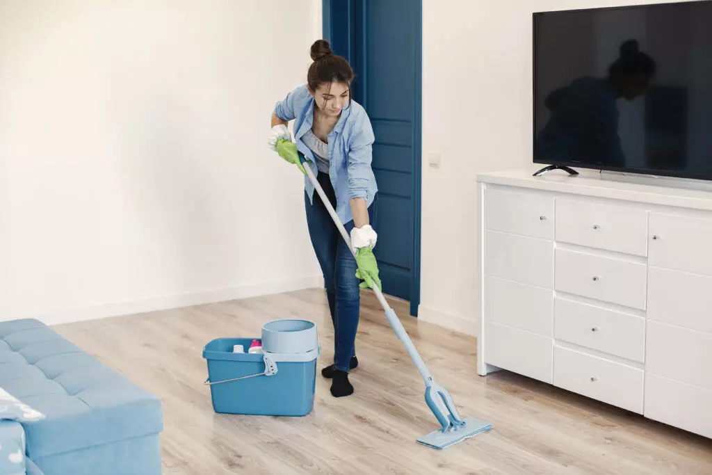 Woman mopping the floor in a tidy living room, part of a professional maid service.