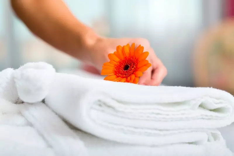 A person placing an orange gerbera daisy on a stack of white towels after a deep cleaning.