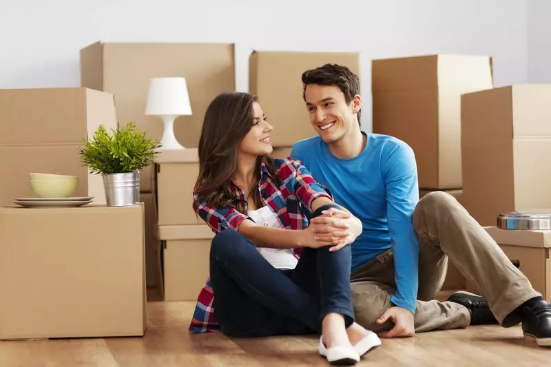 A couple sitting on the floor amidst moving boxes in their new Bay Area home, appearing content and connected.